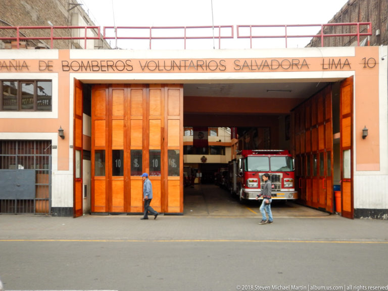 Salvadora Lima No. 10 volunteer fire station with open wooden bay doors, red fire engine, and pedestrians.