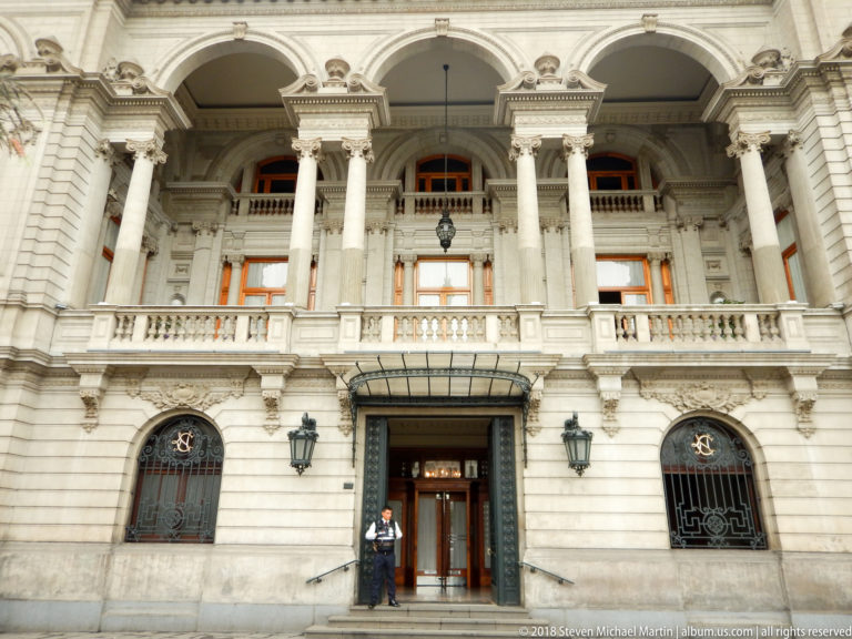 Monumental entrance with glass canopy, iron grilles, paired columns, arches, and balustraded upper level in Lima.