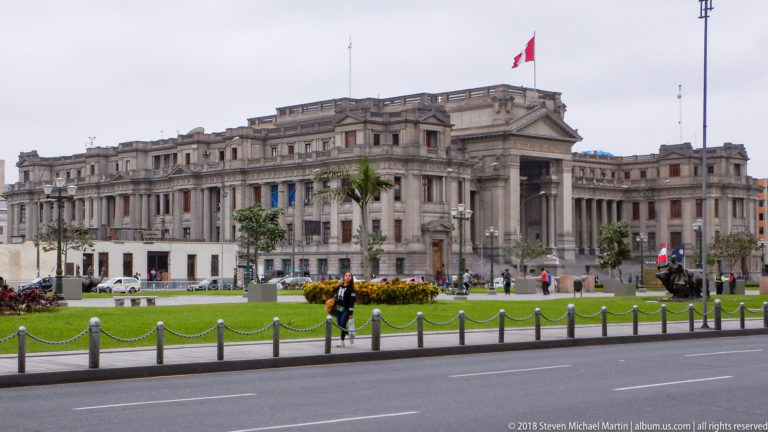 Palace of Justice in Lima with monumental stone façade, central colonnade, landscaped lawn, and Peruvian flag.