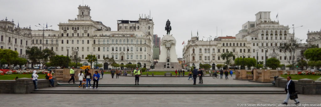 Wide view of Plaza San Martín with pedestrians, gardens, white historic buildings, and the equestrian monument centered in the distance.