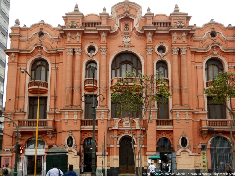 Salmon-colored historic façade with arched windows, small balconies, pilasters, and elaborate roofline ornament in central Lima.