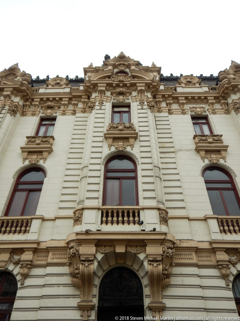 Centered close view of an ornate white monumental façade with arched entrance, balconies, tall windows, and elaborate cresting.