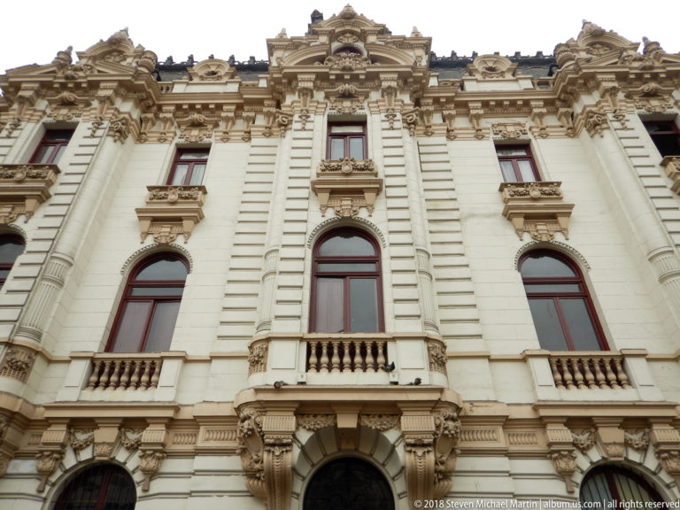 Low-angle close view of an ornate white civic façade with arched windows, balconies, sculpted brackets, and elaborate roofline.