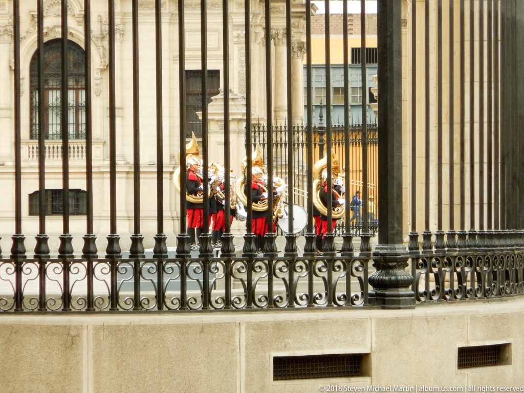 Ceremonial guards in red uniforms seen through closely spaced black iron bars at the Government Palace.