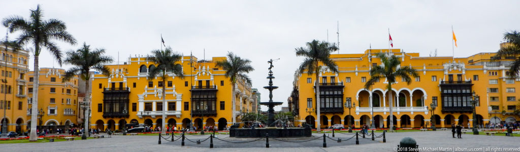 Wide Plaza Mayor view with central fountain, palms, ochre façades, dark wooden balconies, and people.