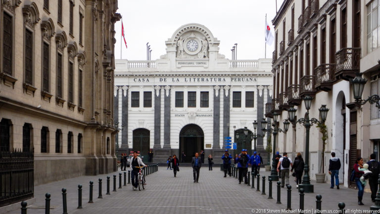 Pedestrian street lined with historic buildings and lamps leading toward the white Casa de la Literatura Peruana.