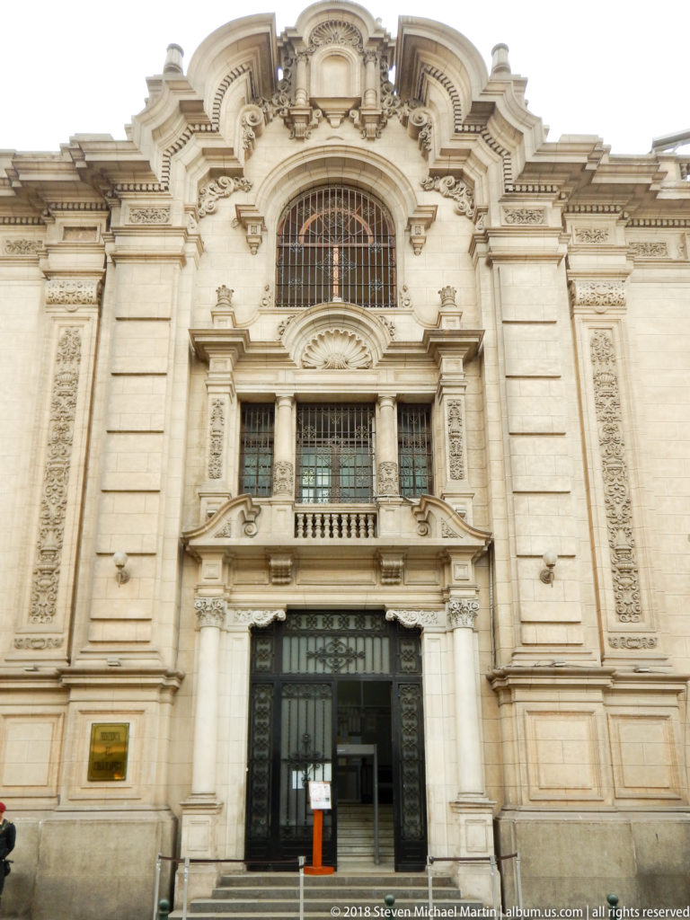 Ornate pale stone entrance with carved panels, pilasters, small balcony, and large arched window above.