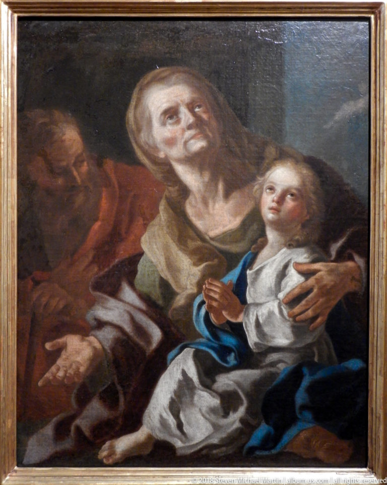 Older woman embraces a young child in white and blue while a bearded man appears in shadow behind them.