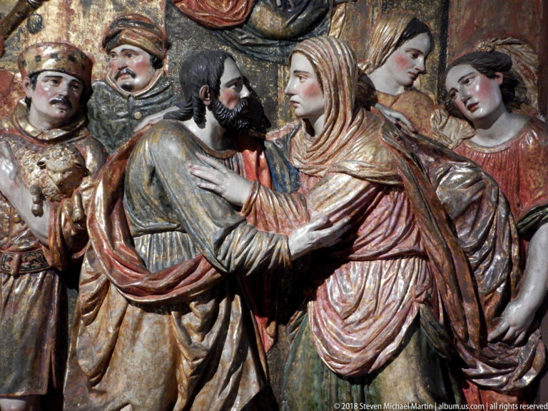 Polychrome relief of a bearded man and veiled woman greeting closely while attendants gather around them.