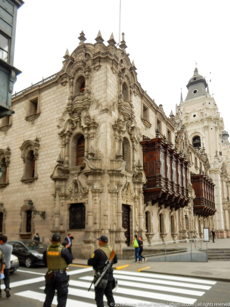 Ornate stone façade of the Archbishop’s Palace with projecting wooden balconies and a cathedral tower beyond.
