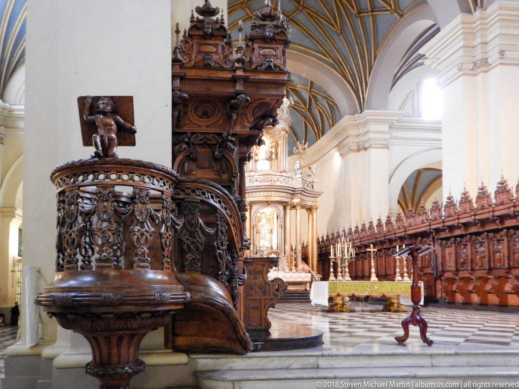 Ornately carved dark wooden pulpit with rounded pierced basket and sculpted base beside the cathedral choir stalls.