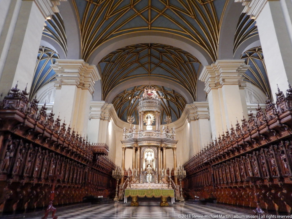 Carved wooden choir stalls flank a central aisle leading toward the sanctuary beneath a patterned ribbed vault.