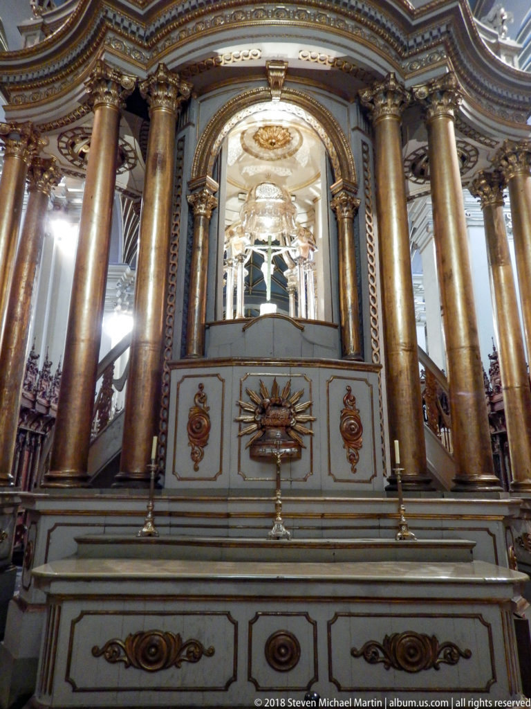 Centered ornate canopy with four tall columns, pale base with gilded emblems, and bright arched interior.