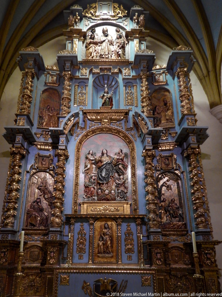 Tall blue-and-gold retablo with spiral columns, large central religious relief, and smaller sculpted panels.