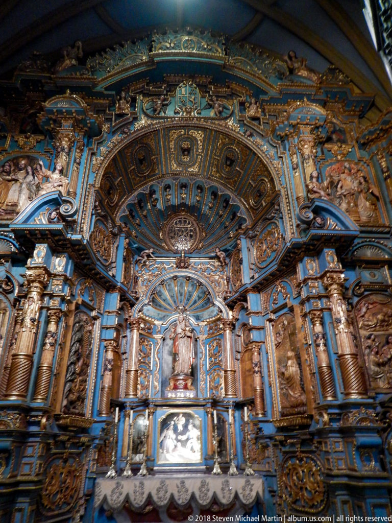 Elaborate blue-and-gold retablo with carved columns, deep coffered canopy, central sacred figure, and altar table.