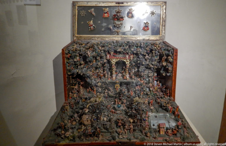 Open box-shaped devotional tableau densely covered with tiny figures, with additional miniature figures mounted inside the raised lid.