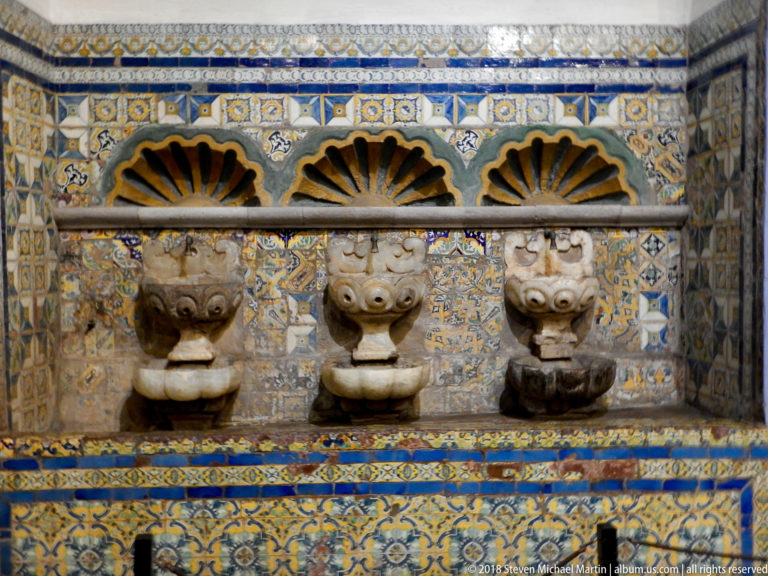 Tiled recess with blue-and-white patterns, three carved stone projecting basins or spouts, and fan-shaped openings above.