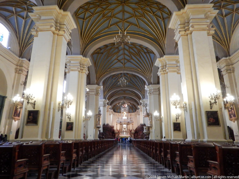 Central nave framed by tall cream piers and dark geometric vaulting, with pews lining the aisle toward the sanctuary.
