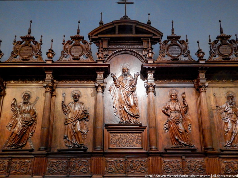 Ornate wooden panel with central standing Christ and four haloed male figures in carved niches.