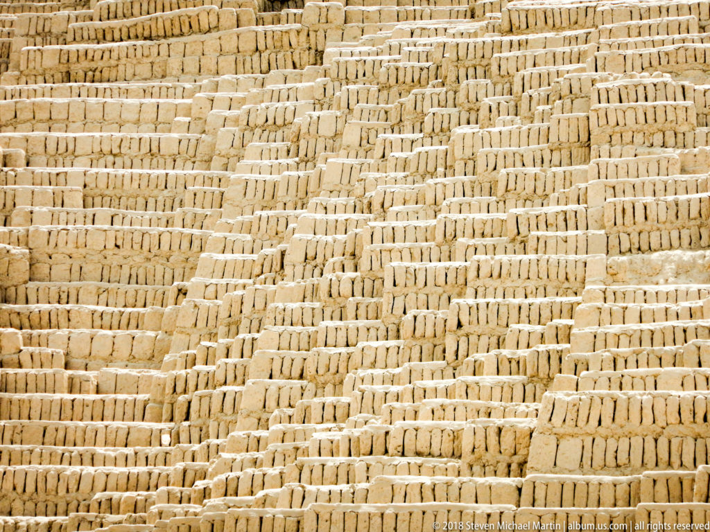 Close view of upright adobe bricks arranged in dense bookshelf-style rows with irregular joints and stepped courses.