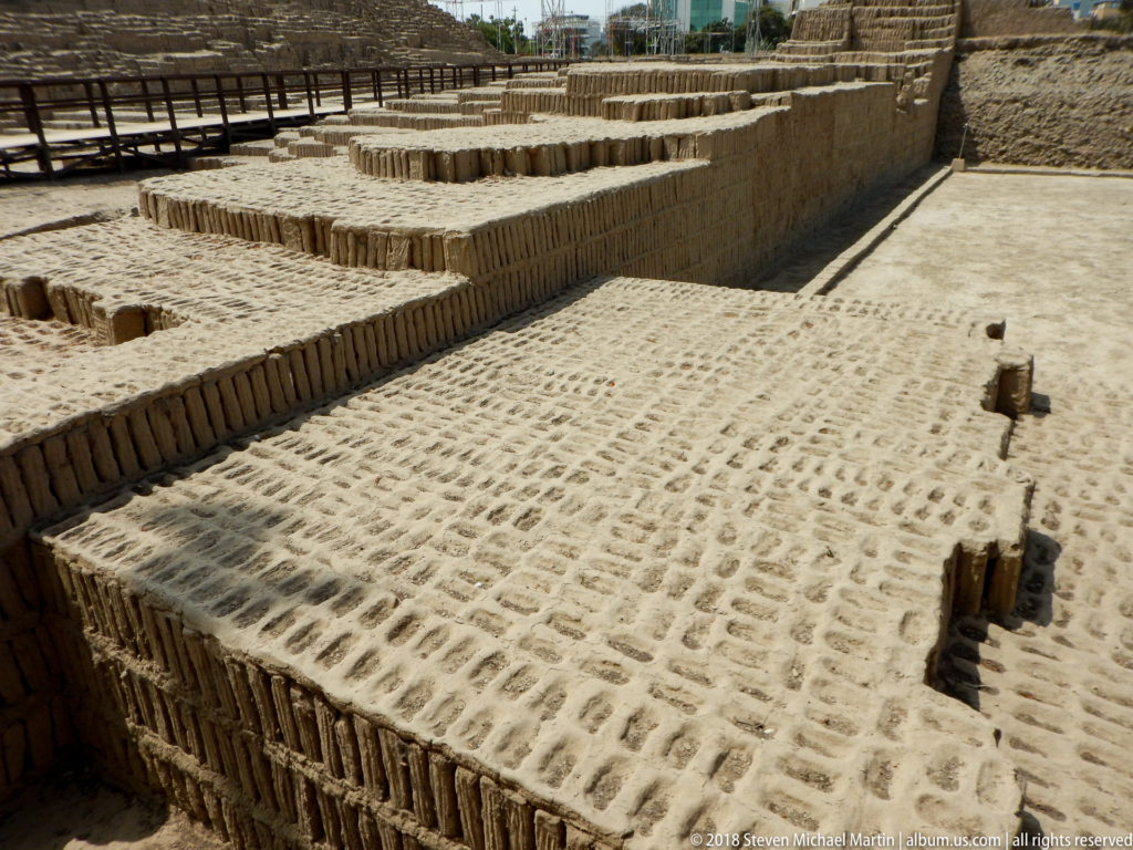 Excavated Huaca Pucllana terraces and walls built from upright adobe bricks, with a broad earthen floor in the foreground.