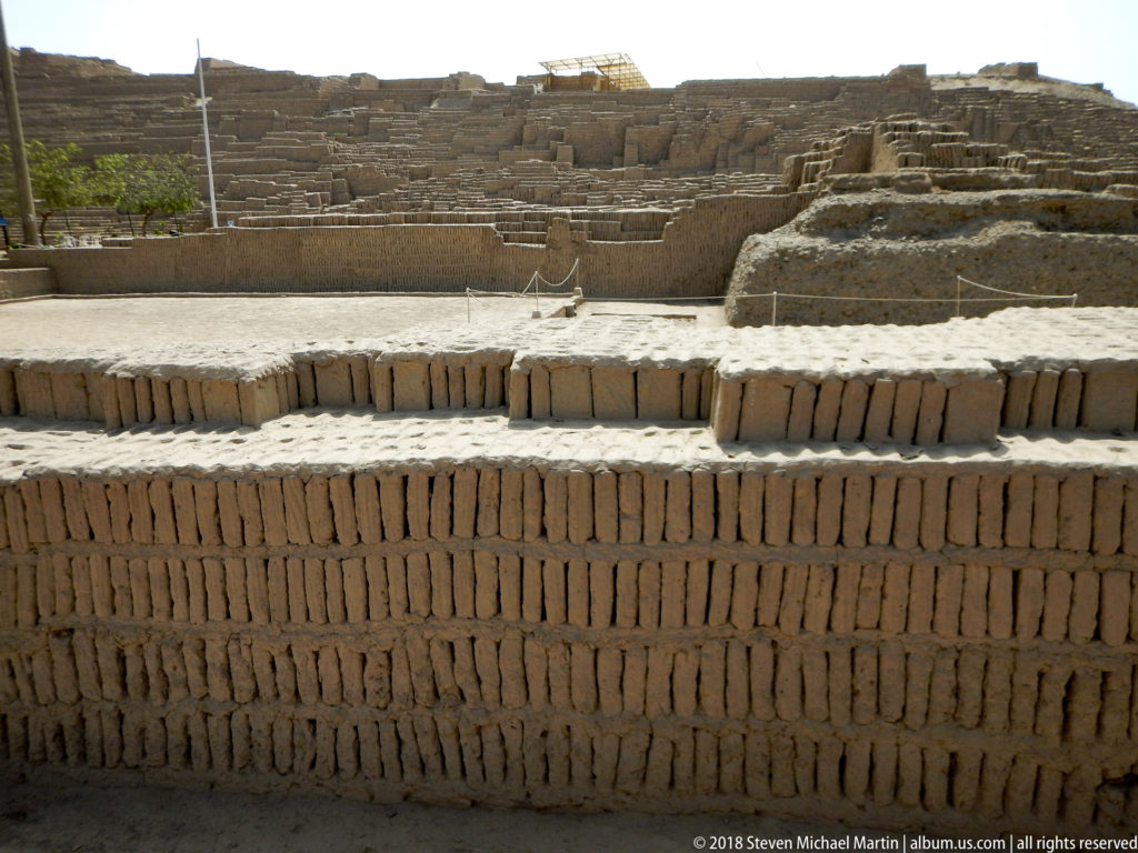 Wide view of layered adobe platforms and low walls rising through the archaeological complex at Huaca Pucllana.