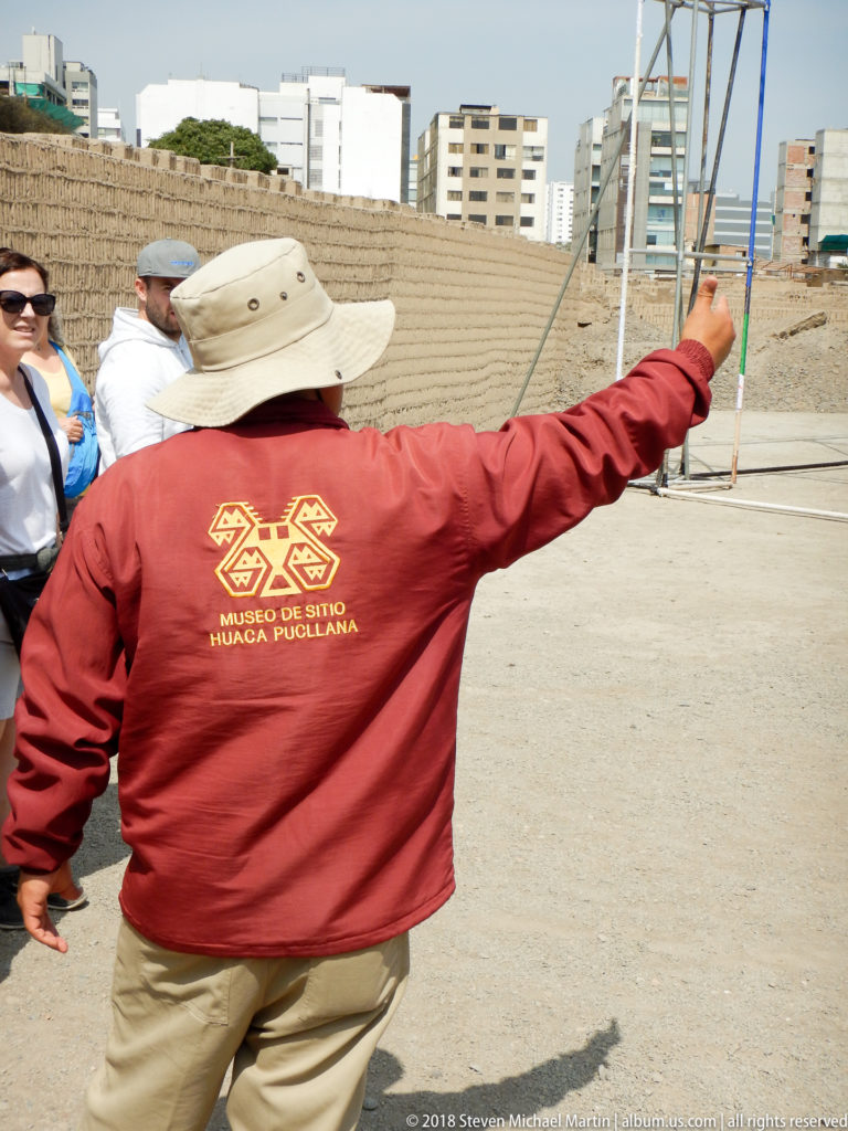 Huaca Pucllana guide in a red museum jacket pointing across the site while visitors stand nearby during a tour.