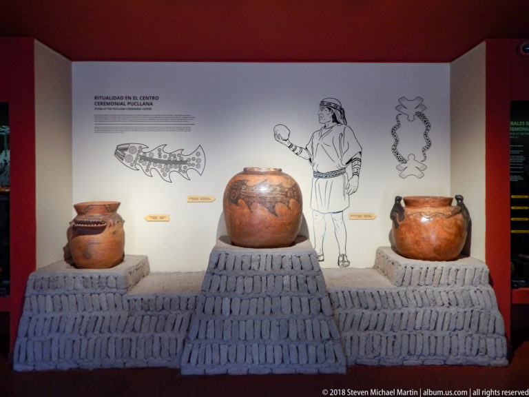 Museum case with several ceramic vessels arranged above a reconstructed platform of upright adobe bricks and interpretive wall graphics.