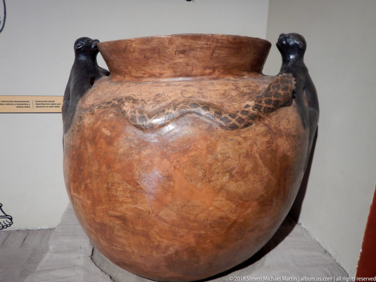 Large reddish ceramic vessel with open rim, dark modeled handles, and a wavy serpent-like appliqué across the shoulder.