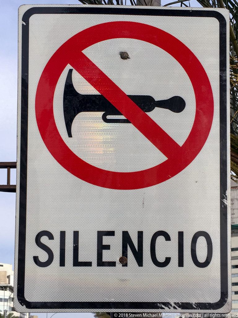 Road sign with a crossed-out black horn symbol above the large word “SILENCIO.”
