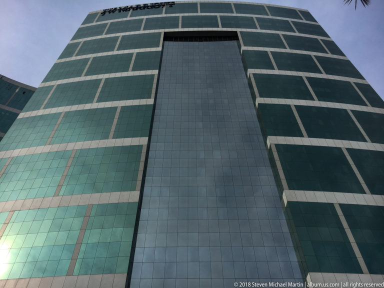 Upward view of a green-glass high-rise with pale horizontal bands and a tall dark recessed bay.