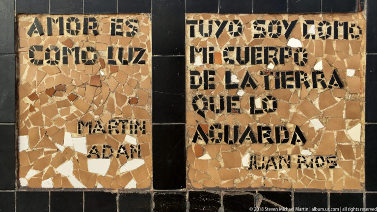 Close detail of black Spanish lettering set into tan broken-tile mosaic panels separated by glossy dark tile bands.