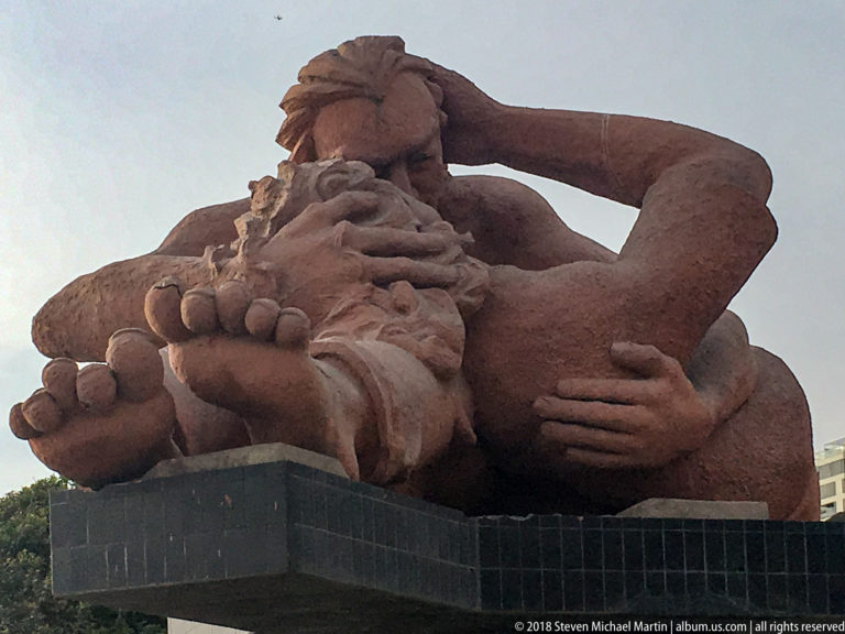 Low-angle view of Víctor Delfín’s El Beso, a reddish-brown monumental sculpture of an embracing couple at Parque del Amor.