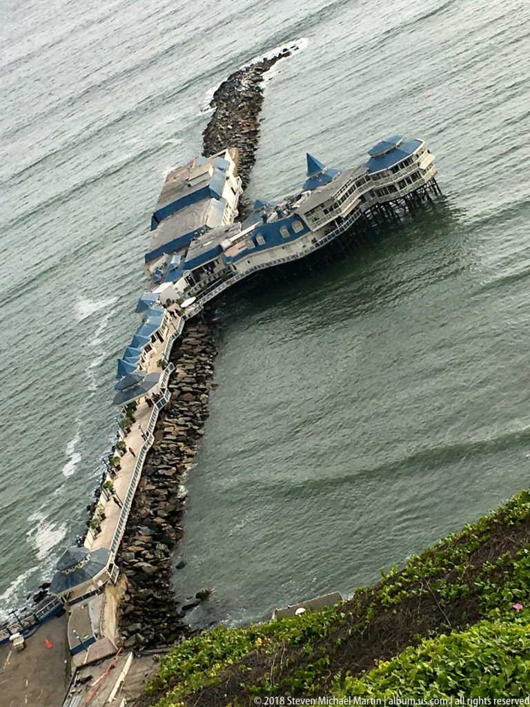 Elevated view of La Rosa Náutica at the end of a long pier and rock breakwater, surrounded by Pacific water below Miraflores.