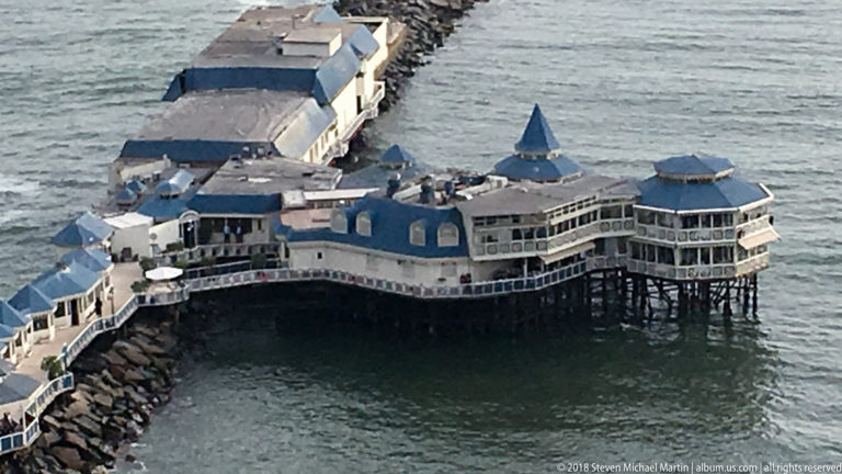 La Rosa Náutica restaurant on pilings over the Pacific, with blue-gray roofs and a causeway extending from the Miraflores shoreline.