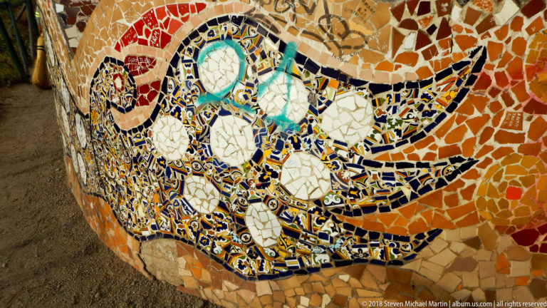 Close mosaic detail of blue, white, turquoise, and orange ceramic fragments arranged in a curling decorative motif.