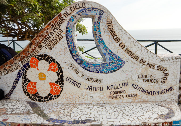 Curved openwork mosaic bench with blue and red tile patterns, names, and inscriptions overlooking the Pacific in Miraflores.
