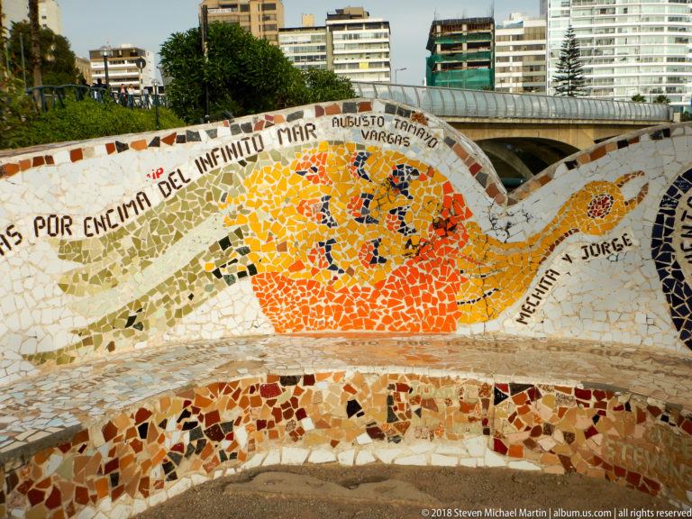 Close view of an orange mosaic medallion, Spanish inscription, and red-and-cream tile fragments on a curved wall.