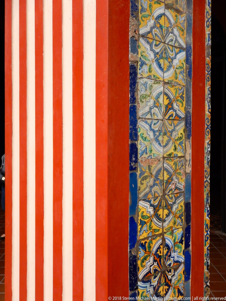 Red-and-white striped cloister pier with a vertical panel of blue, yellow, green, and white patterned glazed tiles.