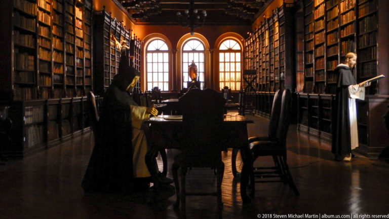Two life-size costumed figures posed among tables and floor-to-ceiling bookcases in Santo Domingo’s historic library.