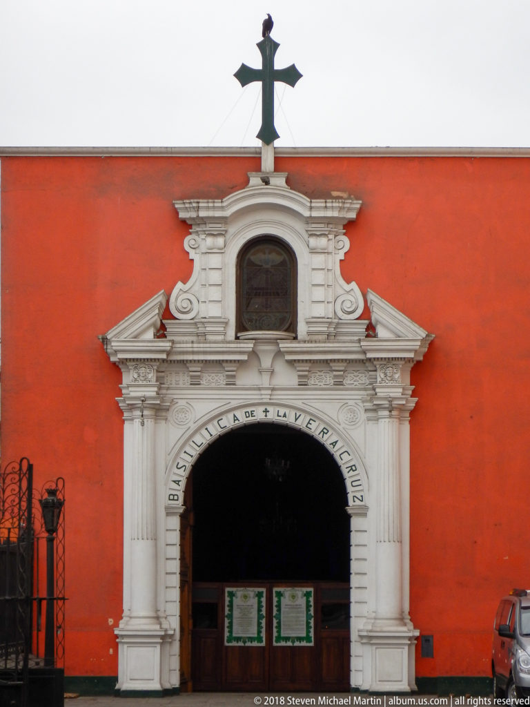 White ornamental portal inscribed Basílica de la Vera Cruz set in a red wall and crowned by a dark cross.