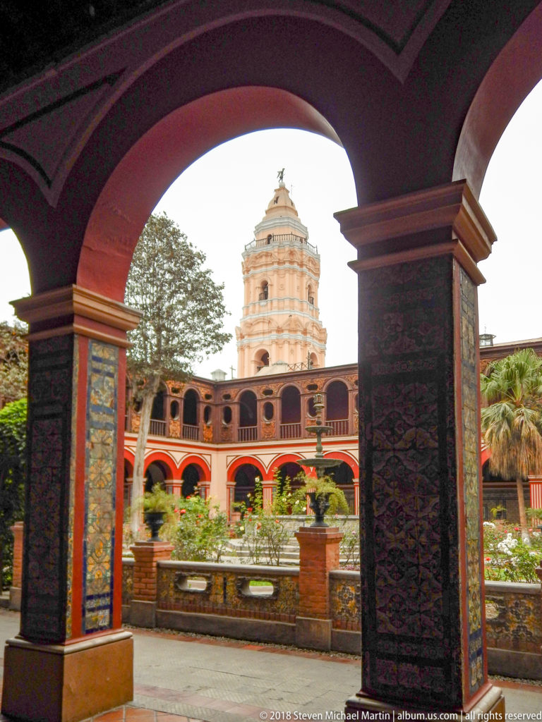Cloister arch framing Santo Domingo courtyard, tiled pier, garden, fountain, arcades, and bell tower beyond.