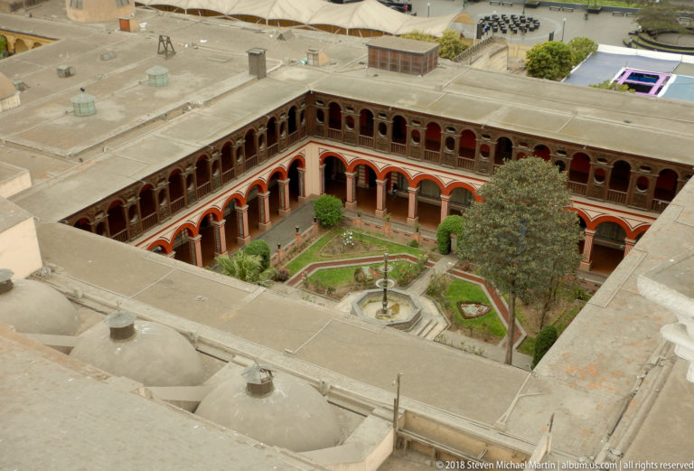 Elevated view of Santo Domingo’s main cloister with arcaded galleries, geometric garden beds, central fountain, and surrounding roofs.