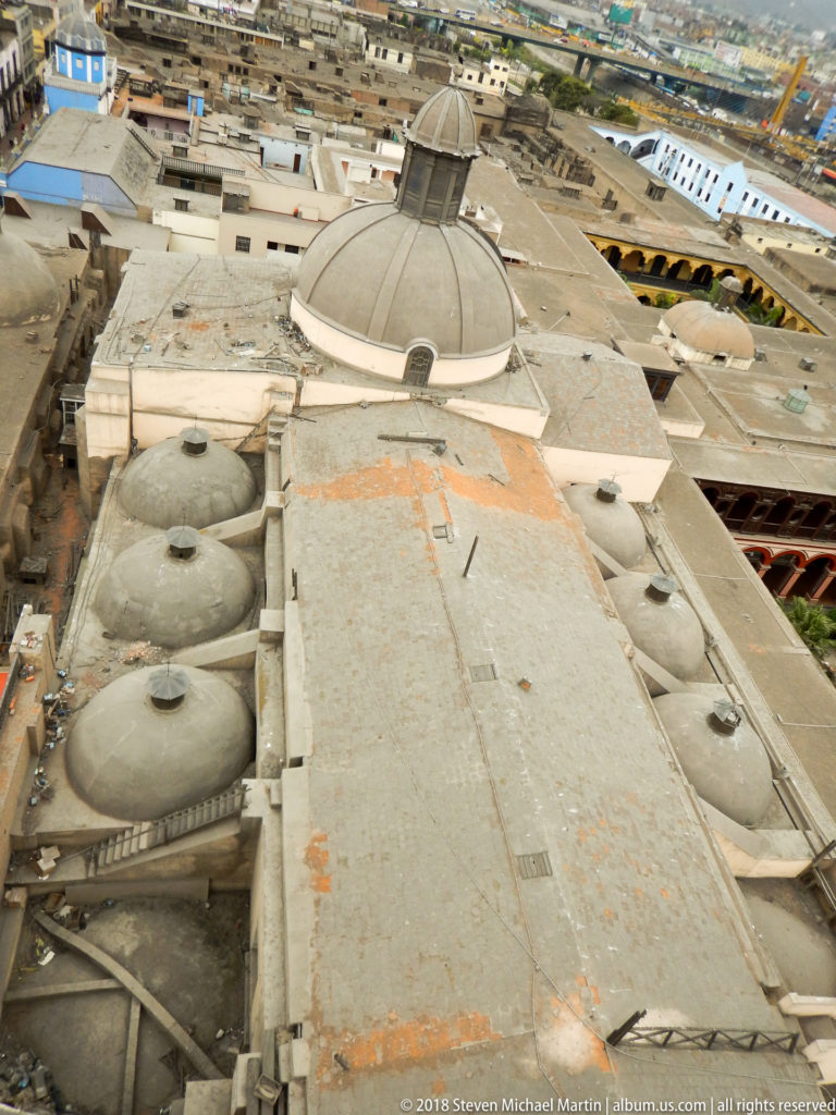 Steep overhead view of Santo Domingo roofscape with a large dome, smaller rounded roof forms, and weathered flat roofs.