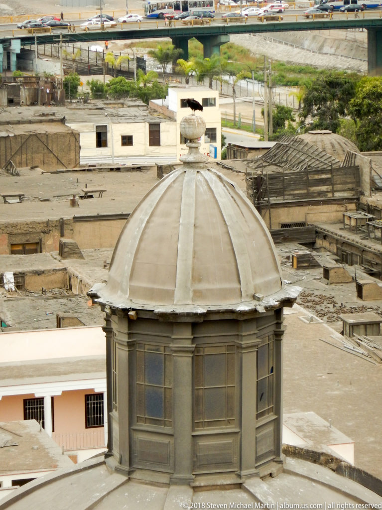 Small gray polygonal dome with tall windows and shallow pilasters rising above the roofs of the Santo Domingo complex.