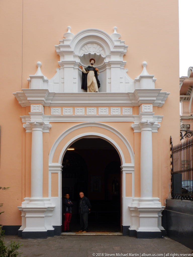 Peach-and-white church portal with broad arch, classical pilasters, and statue of Saint Dominic above the entrance.