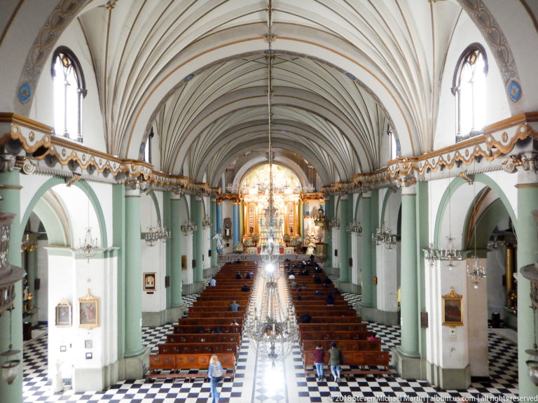 Elevated view down Santo Domingo’s nave with wooden pews, green-and-white arches, vaulted ceiling, and high altar beyond.
