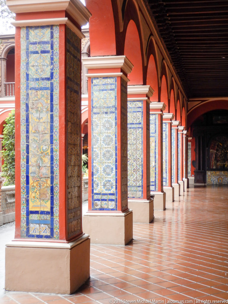 Oblique view along Santo Domingo cloister with red arches and columns covered in blue, yellow, and white glazed tiles.