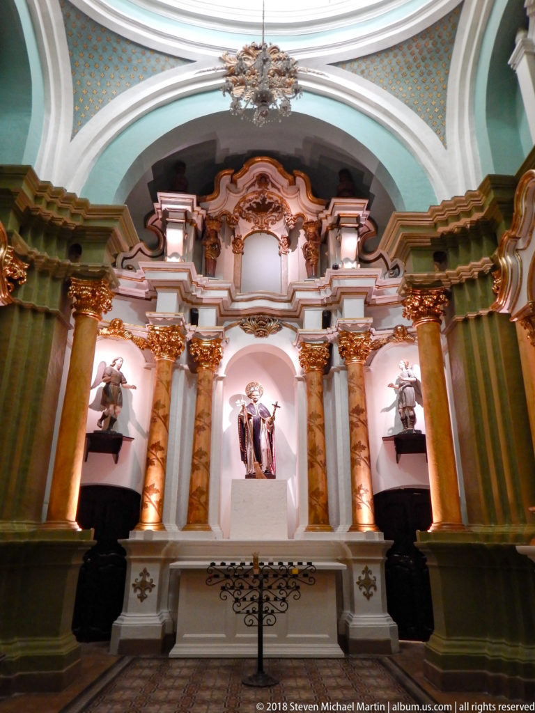 Ornate altar with paired columns, gilded capitals, green wall panels, and a central Dominican saint statue flanked by smaller figures.