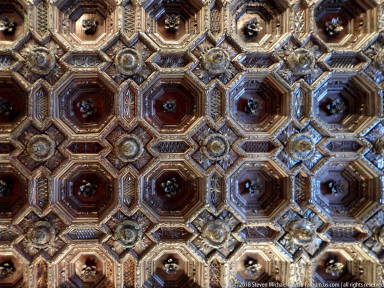 Close view of an ornate wooden coffered ceiling with octagonal compartments, carved rosettes, and gilded geometric moldings.